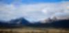Sharp Sawtooth Mountains separate a forrest of evergreen trees and a cloudy blue sky