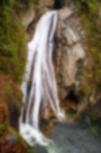 White waterfall stumbles over rock cliff with moist vegetation edges